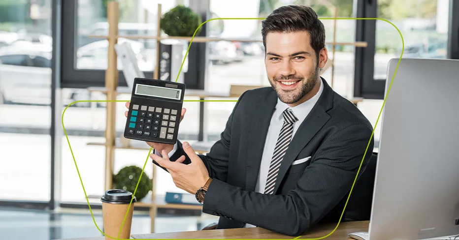 Homem de terno sorrindo num escritório envidraçado, mostrando uma calculadora para a câmera