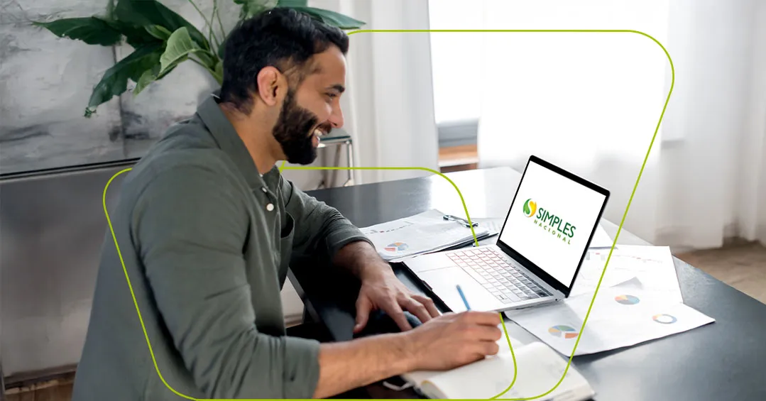 Homem sorrindo enquanto anota num caderno, com o notebook aberto na tela do Simples Nacional